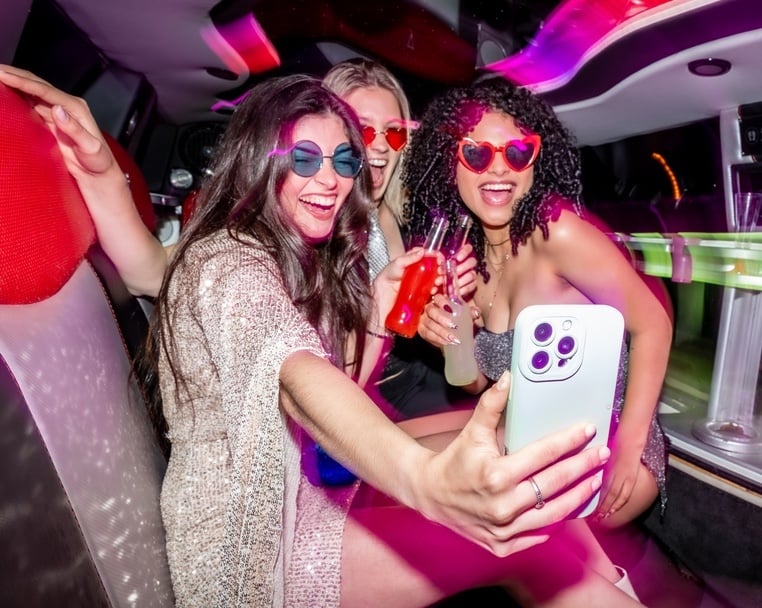 Three women in the back of a limo celebrating and taking their photo with a smart phone