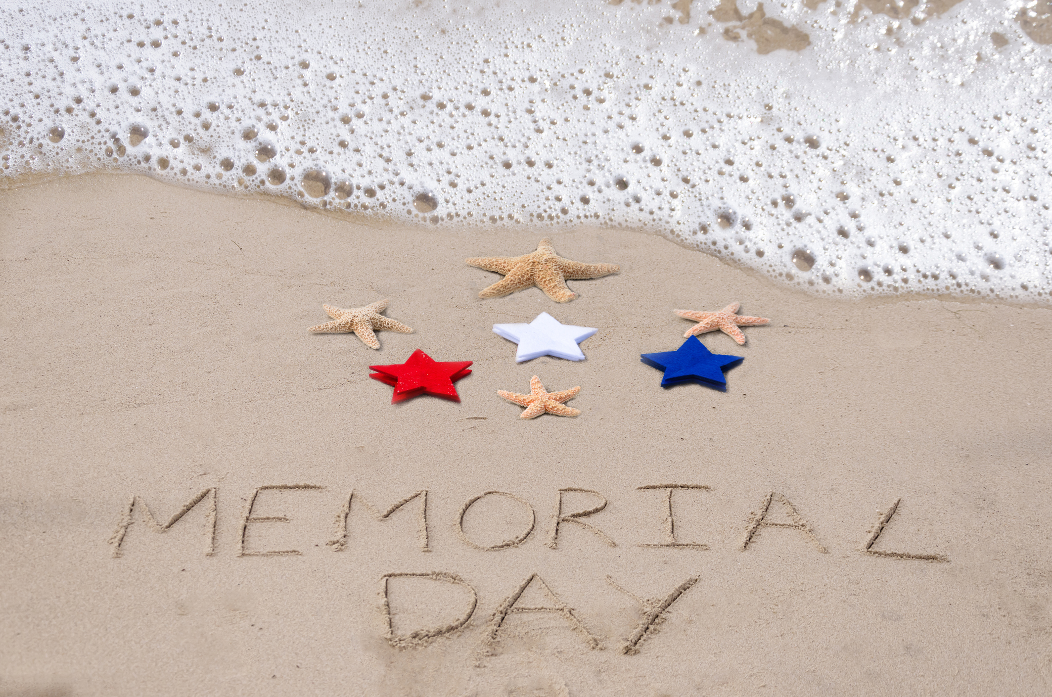 Surf at beach with Memorial Day written in sand and red, white, and blue star fish